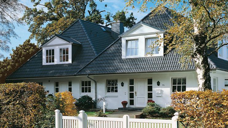 Elegantes zweigeschossiges Haus mit Satteldach, umgeben von Garten und weißem Zaun. Großer Eingangsbereich sichtbar.