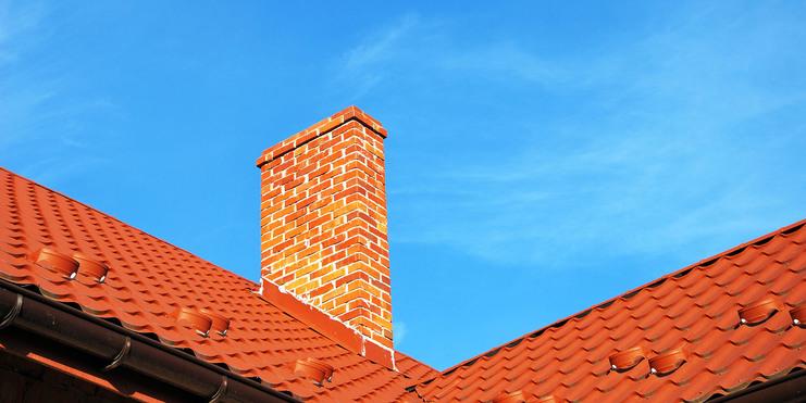Ziegelstein-Schornstein auf einem roten Dach vor klarem, blauem Himmel.