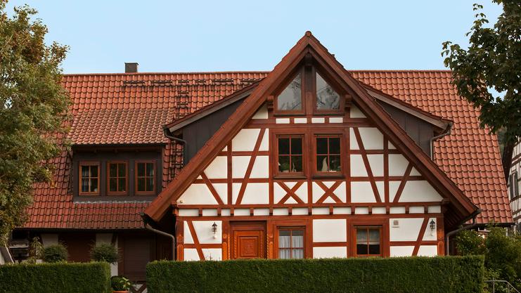 Fachwerkhaus mit roten Ziegeldach, weißen Wänden und grünem Strauch vor der Fassade.