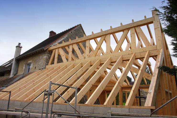 Holzgerüst eines Daches im Bau über einem alten steinernen Gebäude, mit einer Treppe und Holzlatten sichtbar.